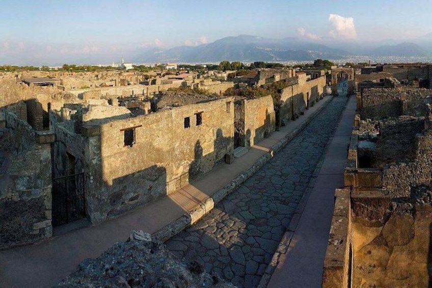 Ancient ruins with stone pathways and walls, a distant mountain range, and a clear sky. 4