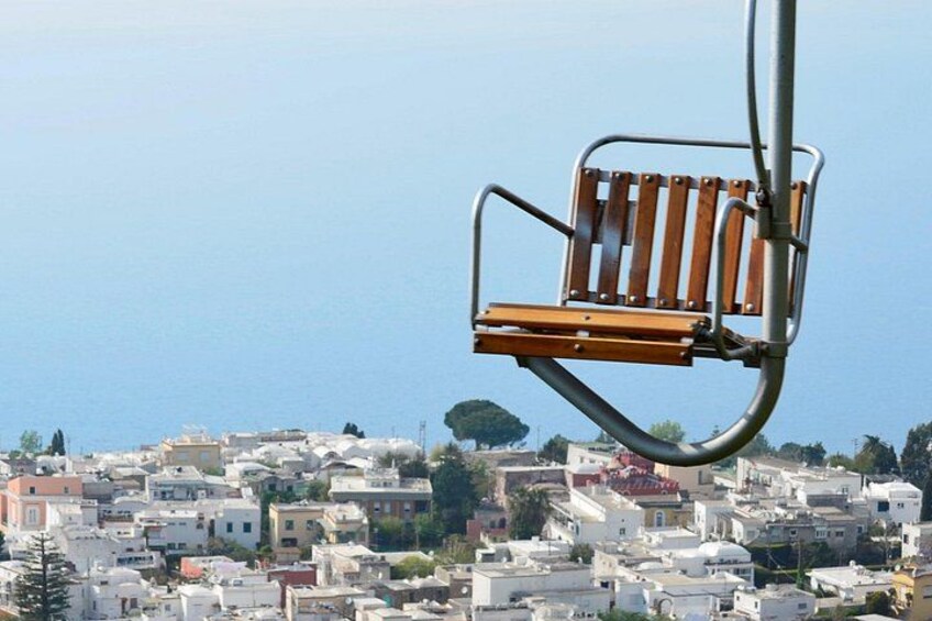 A chair attached to a metal pole overlooking a densely packed urban area with buildings and a clear blue sky. 3