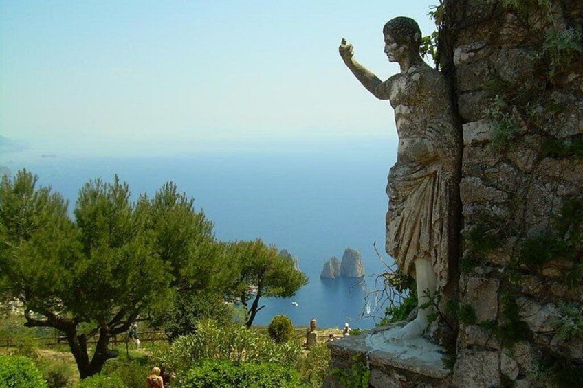 A statue on a cliff overlooking a coastal landscape with trees and a distant view of the sea. 4