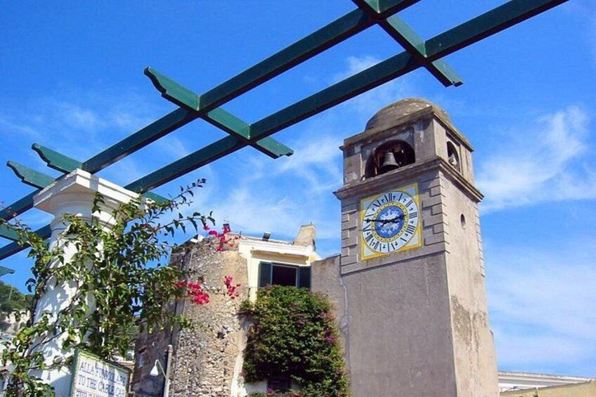 A clock tower with Roman numerals, a clear blue sky, and a green pergola structure. 5