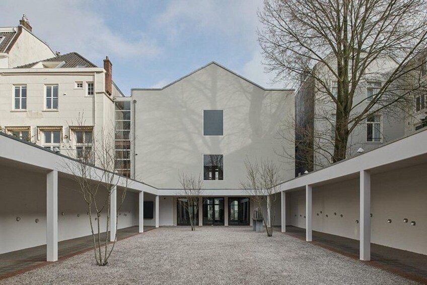 A modern building with a flat roof, a central entrance, and a gravel courtyard surrounded by white walls. 2