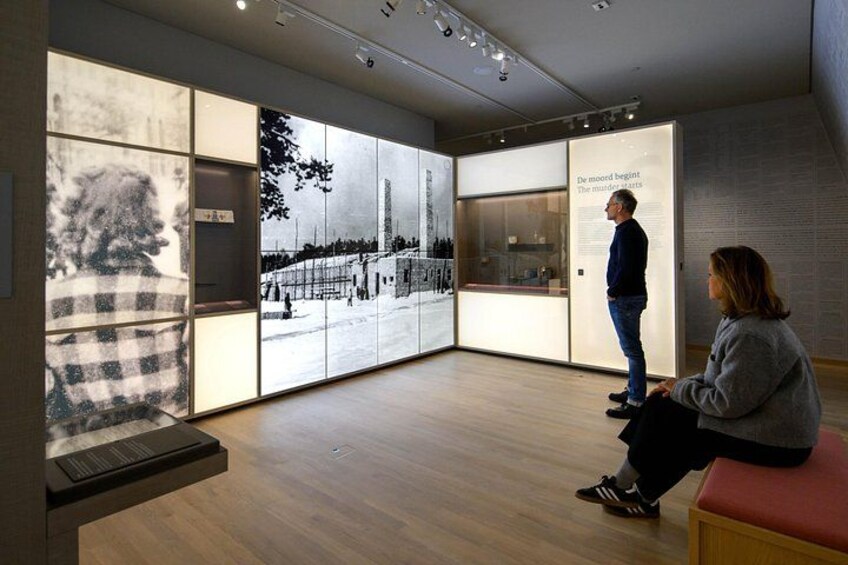 An indoor exhibition space with large display panels, a wooden floor, and a bench. 3