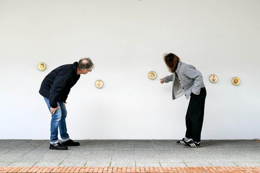 Two people standing on a sidewalk, one bending forward and the other pointing. 4