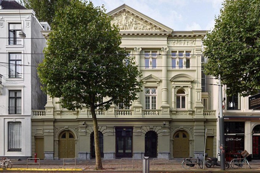 A historic building with ornate architecture, a large tree in front, and bicycles parked nearby. 5