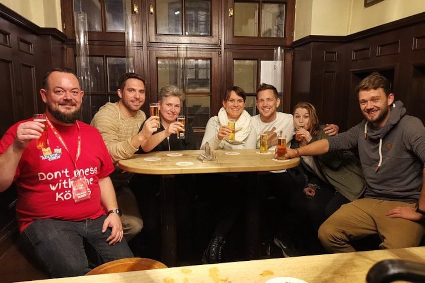 A group of people sitting around a round table in a room with wooden paneling. 5