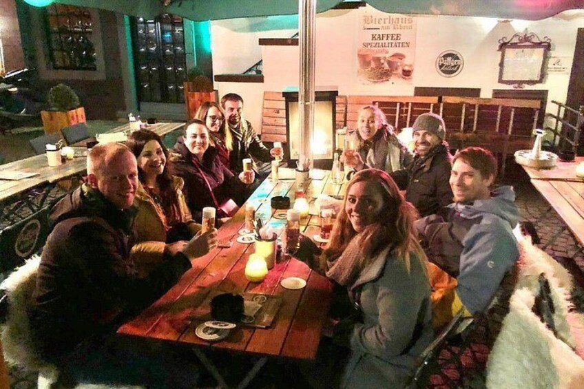 A group of people seated around a wooden table with candles and drinks, in a cozy indoor setting with a sign indicating a coffee shop. 4