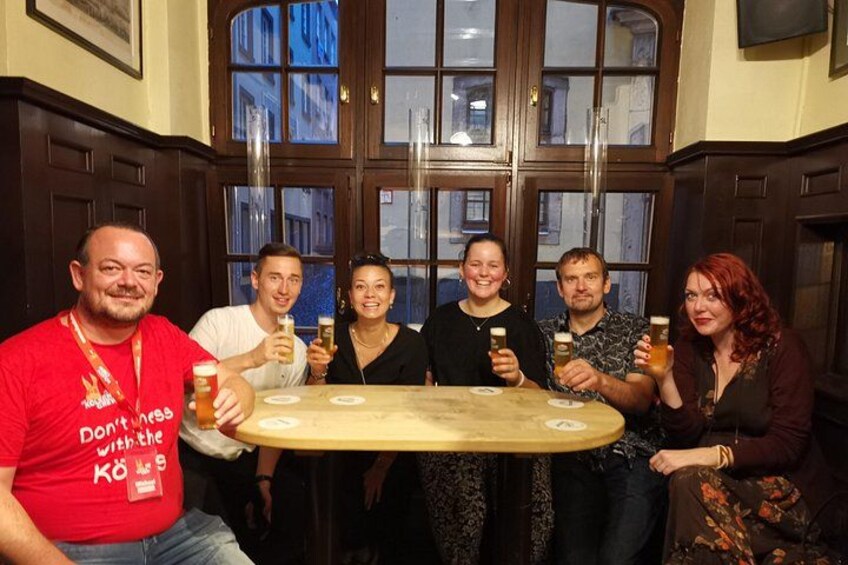 A group of people sitting around a table with drinks, in a room with wooden paneled walls and large windows. 2