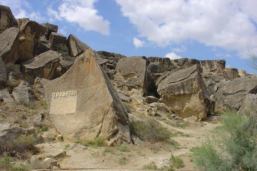 A rocky landscape with a large boulder labeled 'QOBUSTAN' and a clear sky. 4
