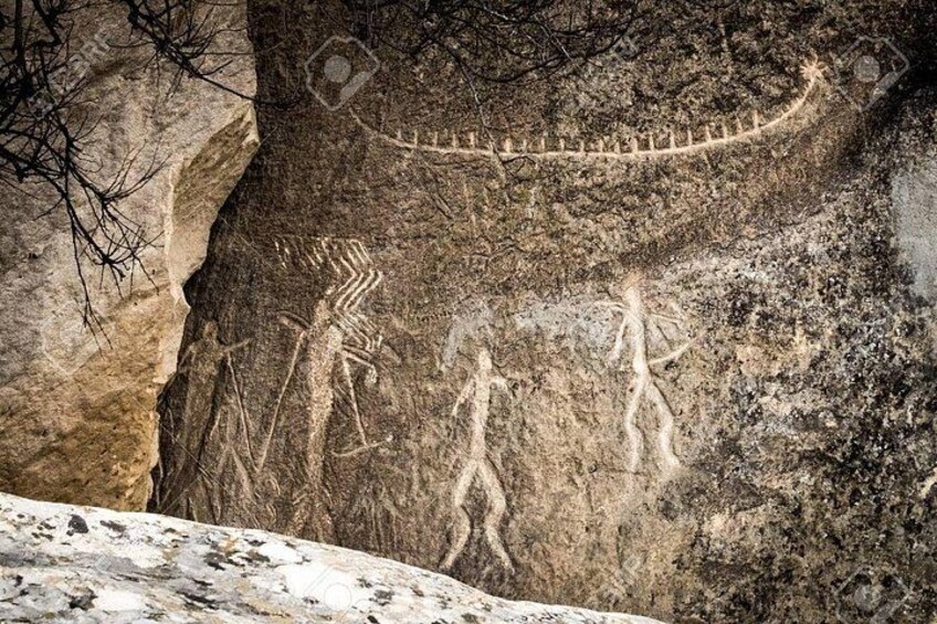 A rock face with ancient carvings, including a human figure and a snake. 3