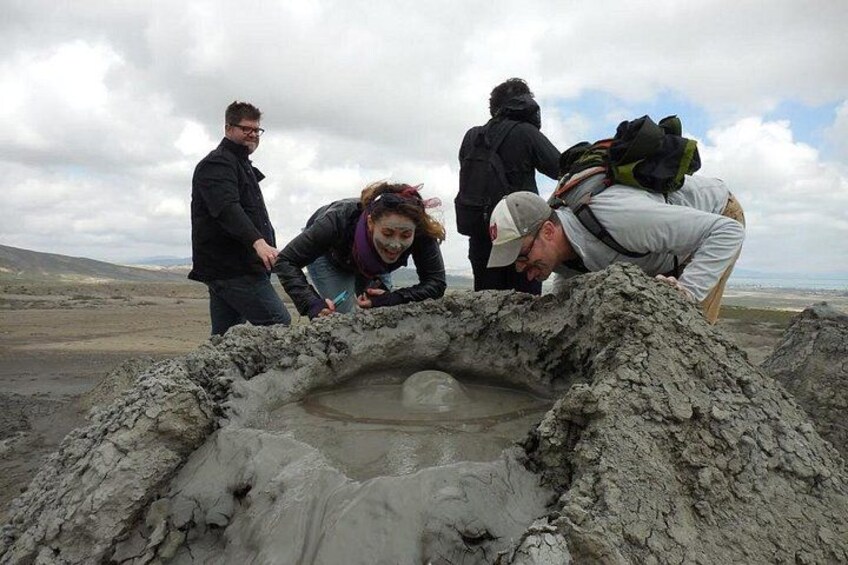 A group of people examining a large, circular, muddy pit in a barren landscape. 2