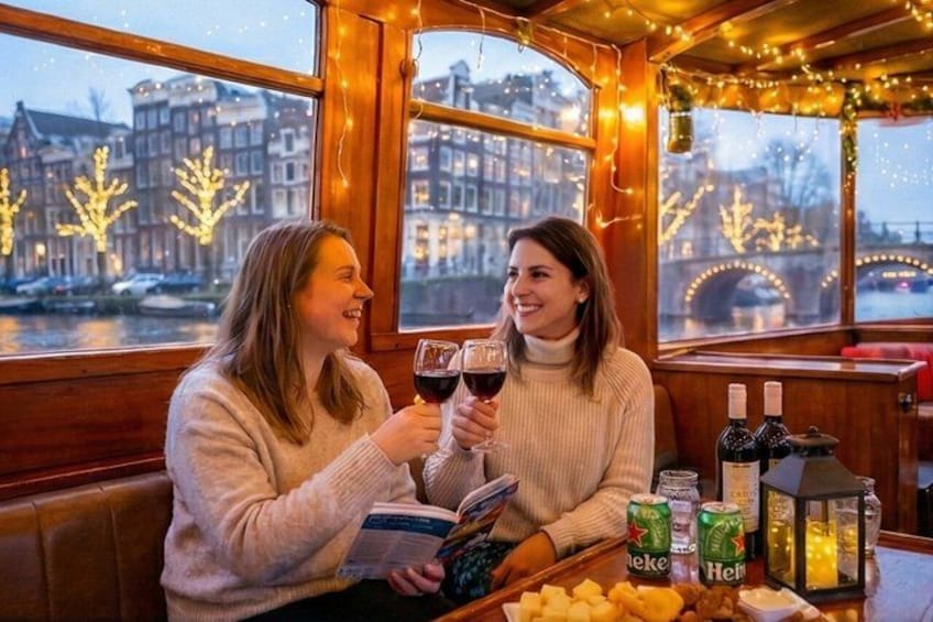 Two people toasting with wine glasses in a cozy, warmly lit room with a view of a river and buildings. 4