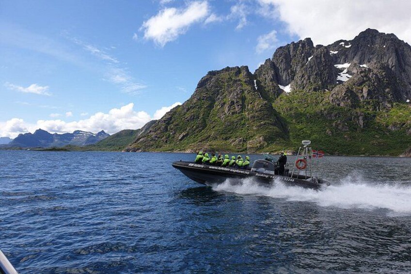 A boat with passengers and a wake behind it, water, and mountains in the background. 3