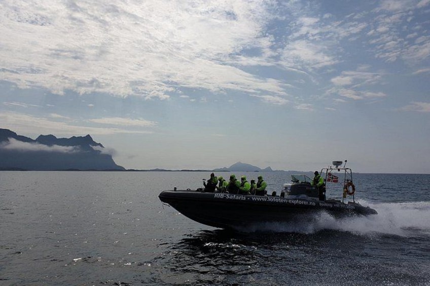 A speedboat with people on board, moving across a body of water with mountains in the background. 2