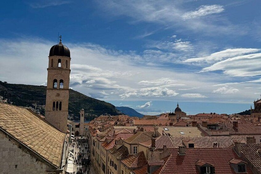 Eine Küstenstadt mit einem markanten Turm, Gebäuden mit Terrakotta-Dächern und blauem Himmel. 3