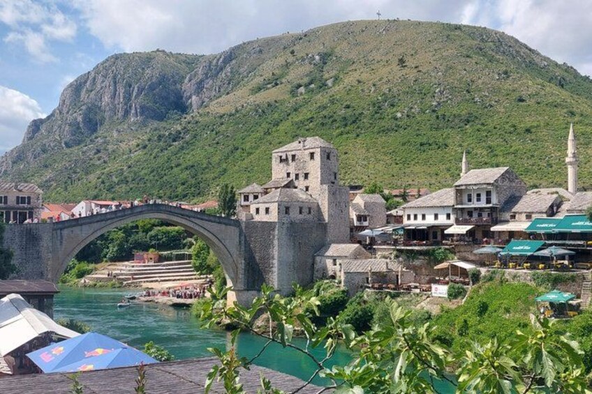 A stone bridge over a river, a town with historic buildings, and a mountain in the background. 3