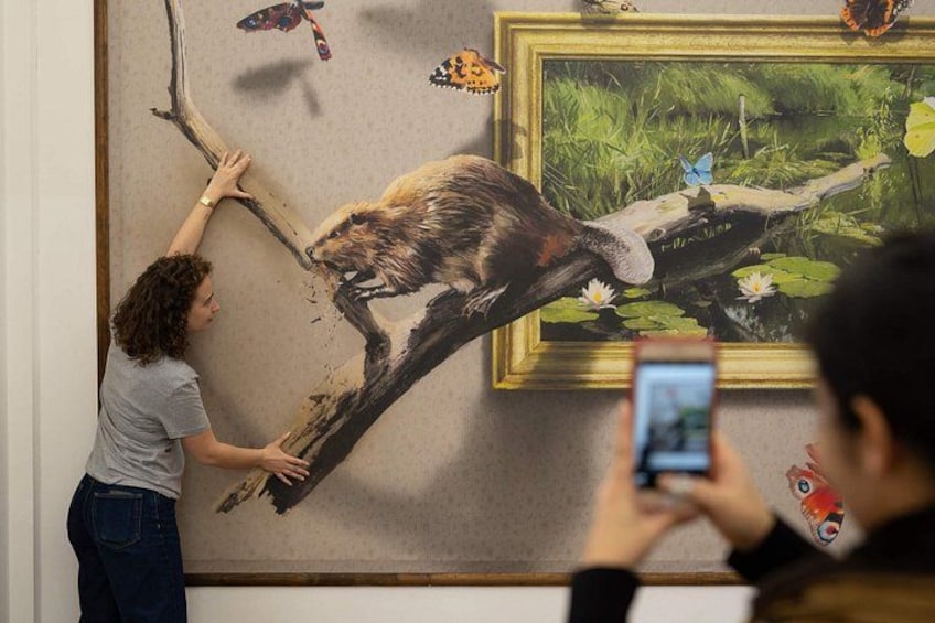 Una persona interactuando con un mural grande, otra persona tomando una fotografía y mariposas en la pared. 5