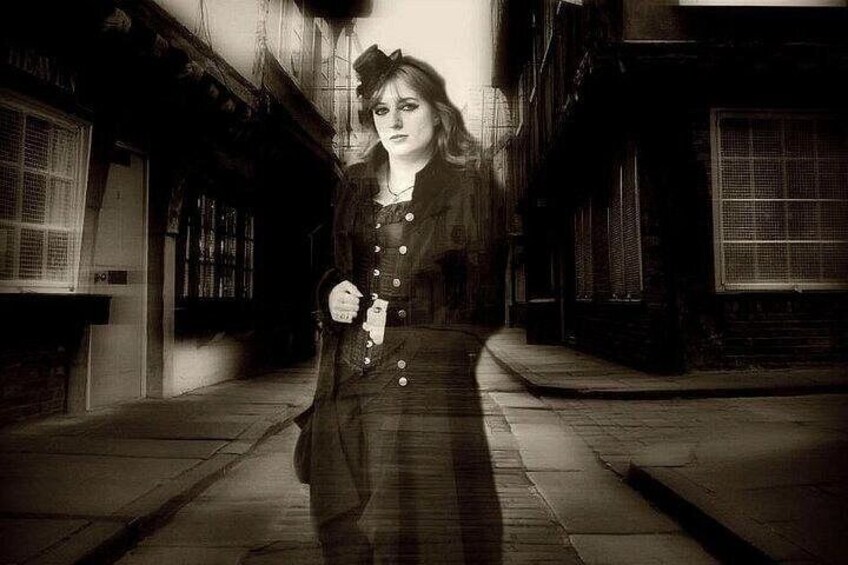A person walking down a dimly lit alleyway with brick buildings and a sign that reads 'HEWES.' 5