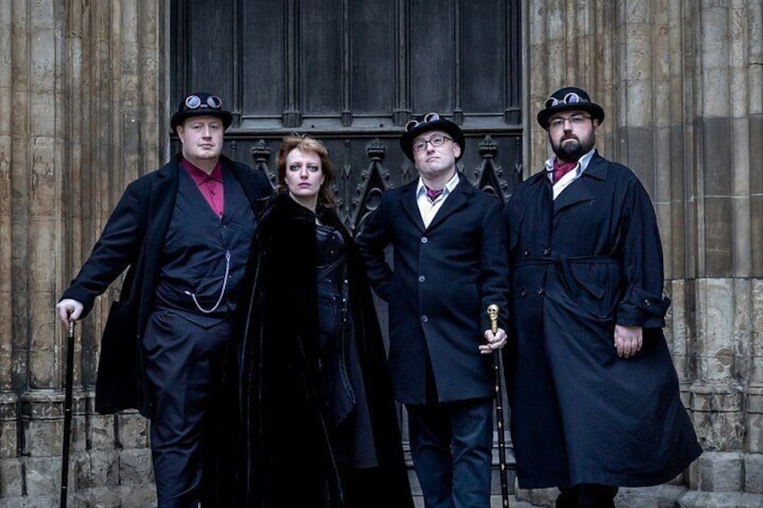 Four people in period clothing standing in front of a building with a large door. 5
