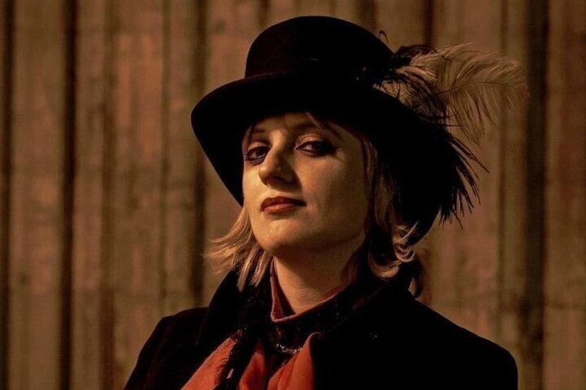 A person wearing a black hat with feathers, a red shirt, and a dark coat. 4