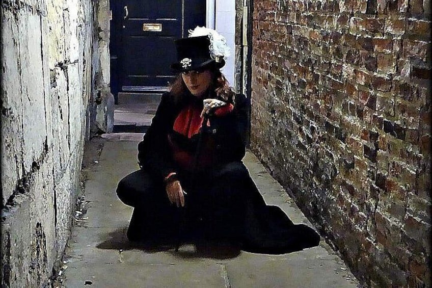 A person crouching in a narrow alleyway with brick walls and a door in the background. 3