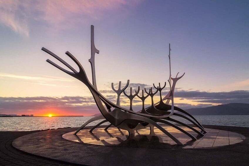 A metal sculpture with tree-like structures, set against a sunset over water. 4