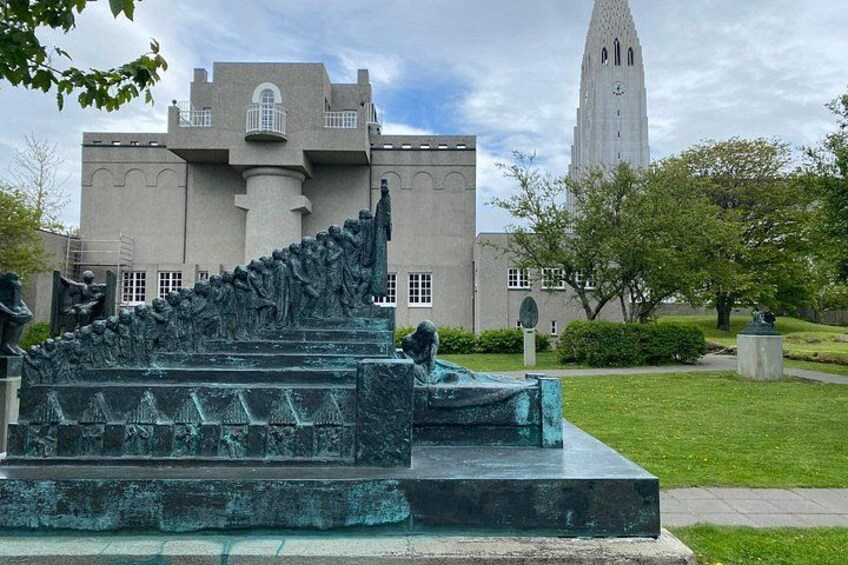 A sculpture of a crowd ascending a staircase, a building with a tower, and a clear sky. 3