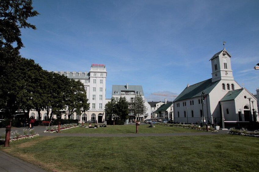A grassy square with a church and a large building with a red sign. 5