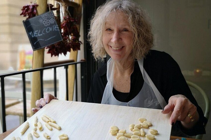 A person holding a large sheet of dough with pasta shapes on it. 2