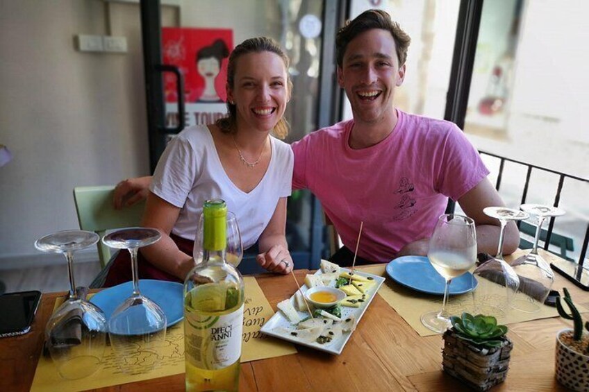 Twee personen zitten aan een tafel met eten, wijn en een wijnfles. 5