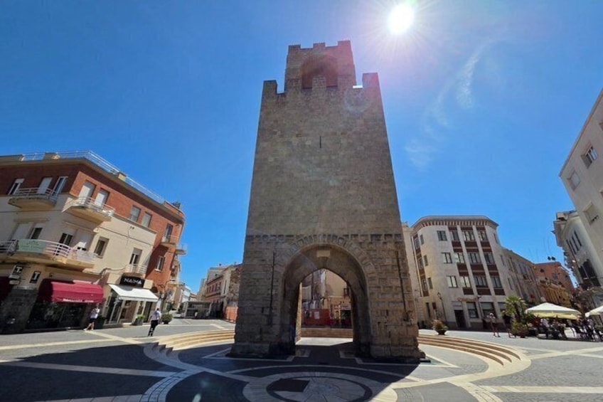 A historic stone tower with an archway, surrounded by modern buildings and a clear blue sky. 5