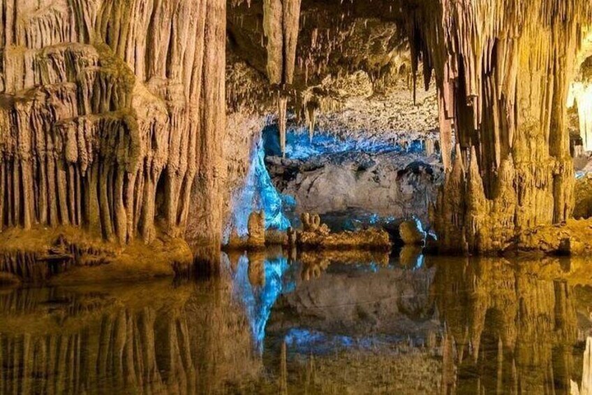 Eine Höhle mit Stalaktiten und Stalagmiten, ein Wasserspiegel, der das Innere der Höhle widerspiegelt, und blaues Licht, das das Wasser beleuchtet. 2