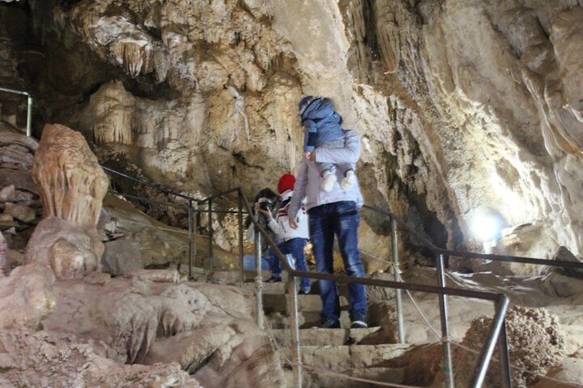 A cave with stalactites and a person carrying a child up a metal staircase. 1