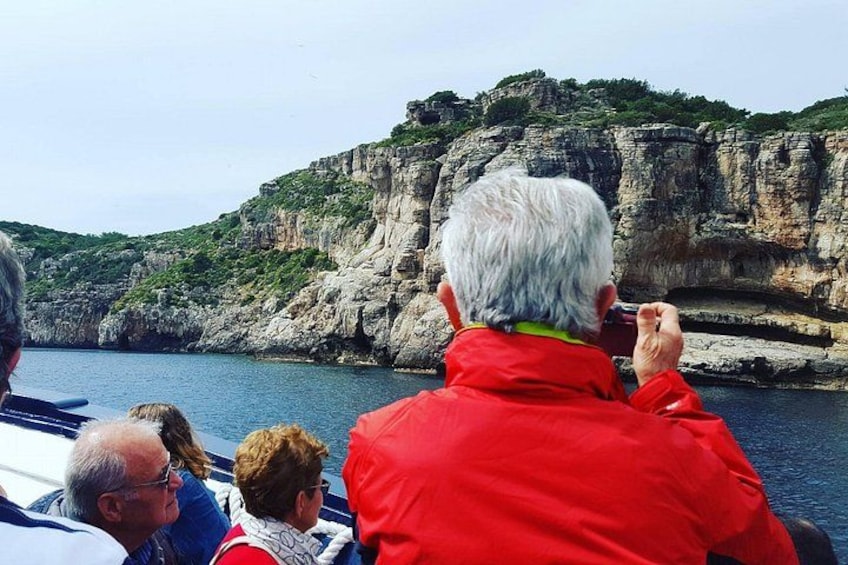 A group of people on a boat, a rocky coastline, and cliffs. 1