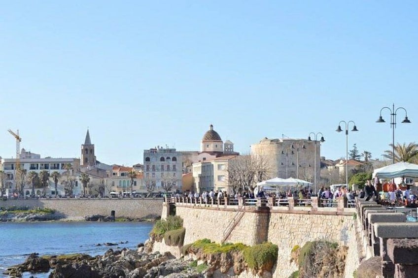 A coastal town with historic buildings, a fortified wall, and a clear blue sky. 5