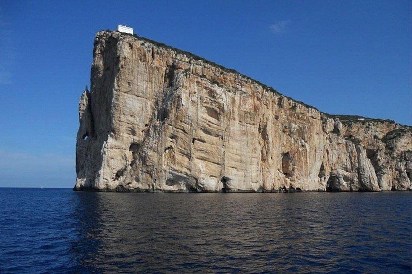 A large limestone cliff by the sea with a small building on top. 3