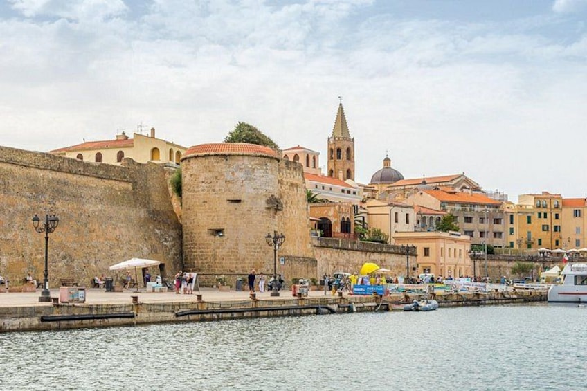 A waterfront cityscape with historic buildings, a prominent tower, and a stone wall. 4