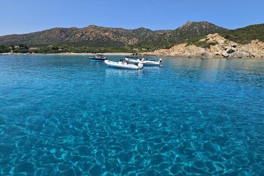 A clear blue sea with boats and rocky hills in the background. 5