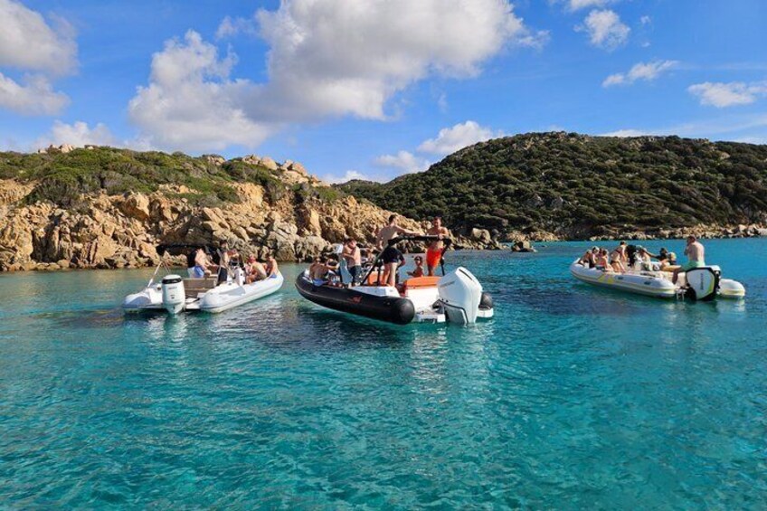 A group of people on small boats in clear blue water, with rocky hills in the background. 2