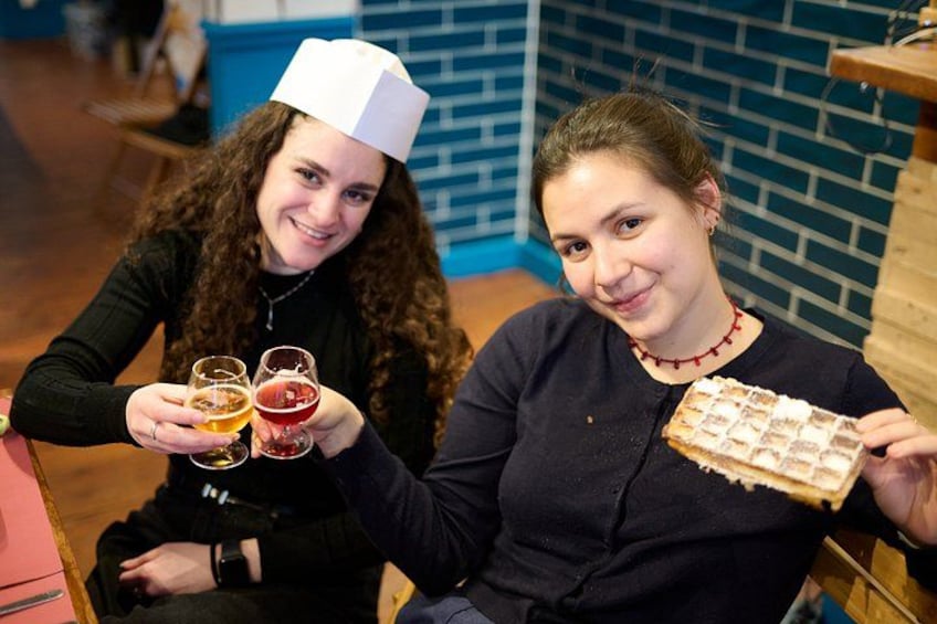 Two people holding glasses of beer and a slice of pizza. 2
