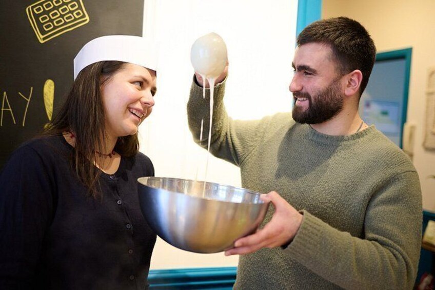 Two people holding a large metal mixing bowl, one person appears to be pouring a liquid from a jug into the bowl. 4