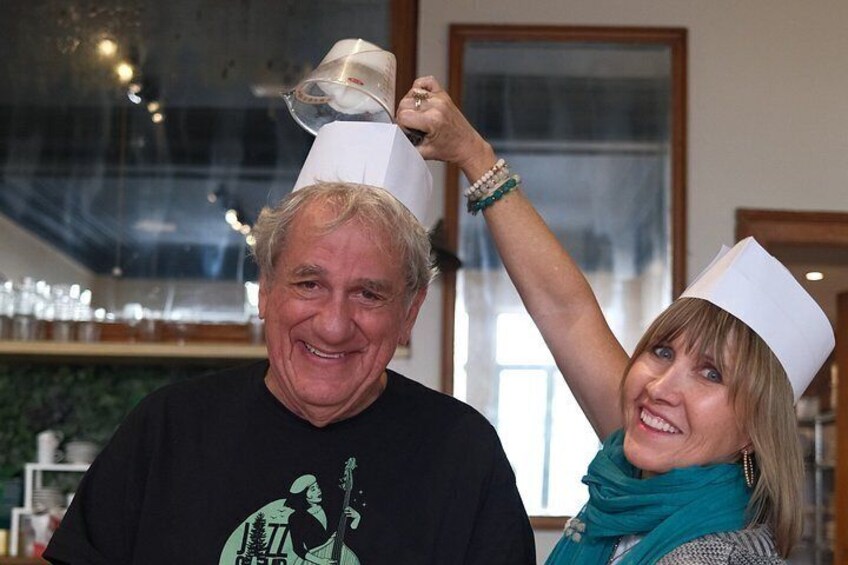 Two people wearing chef hats, one holding a hat above their head. 3