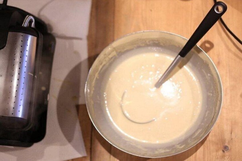 A metal bowl with a whisk, containing a creamy mixture, on a wooden surface. 2