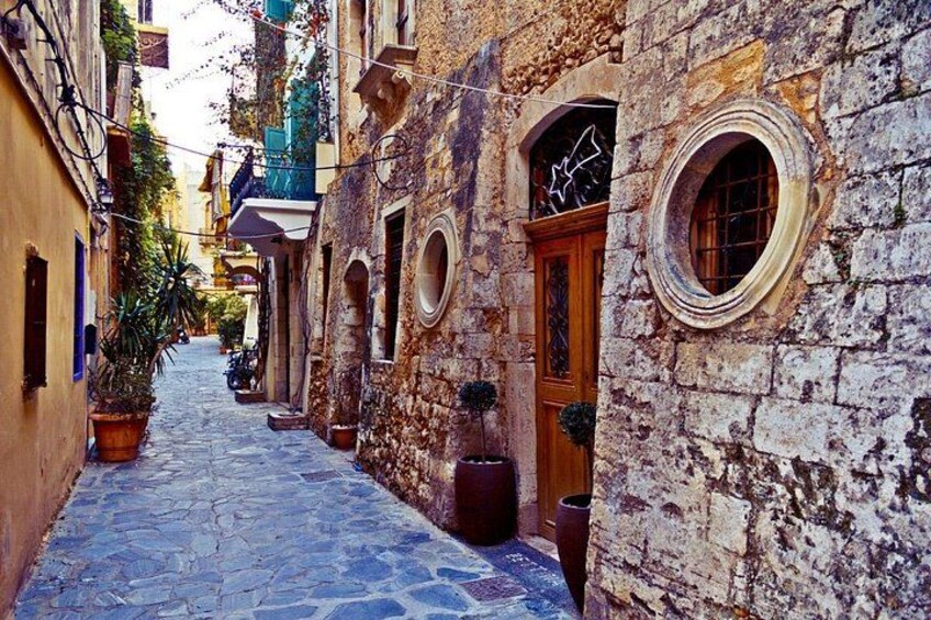 A narrow cobblestone street flanked by historic stone buildings with arched doorways and circular windows. 3