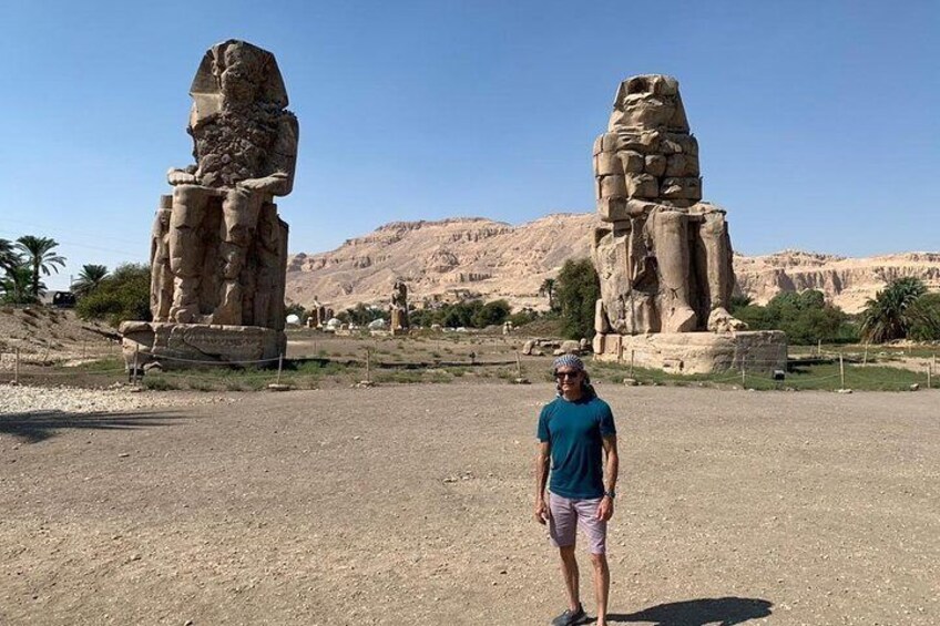 A person standing in front of two large stone statues in a desert landscape. 5