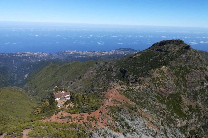 A mountainous landscape with a prominent peak, a small building, and a coastal view in the distance. 4