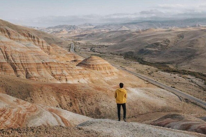 Une personne vêtue d’une veste jaune se tient sur une colline surplombant une vallée parsemée de formations rocheuses en strates. 5