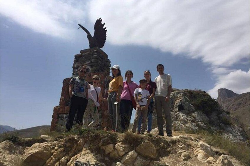 Un groupe de personnes se tient sur un promontoire rocheux, surmonté d’une statue d’aigle. 3