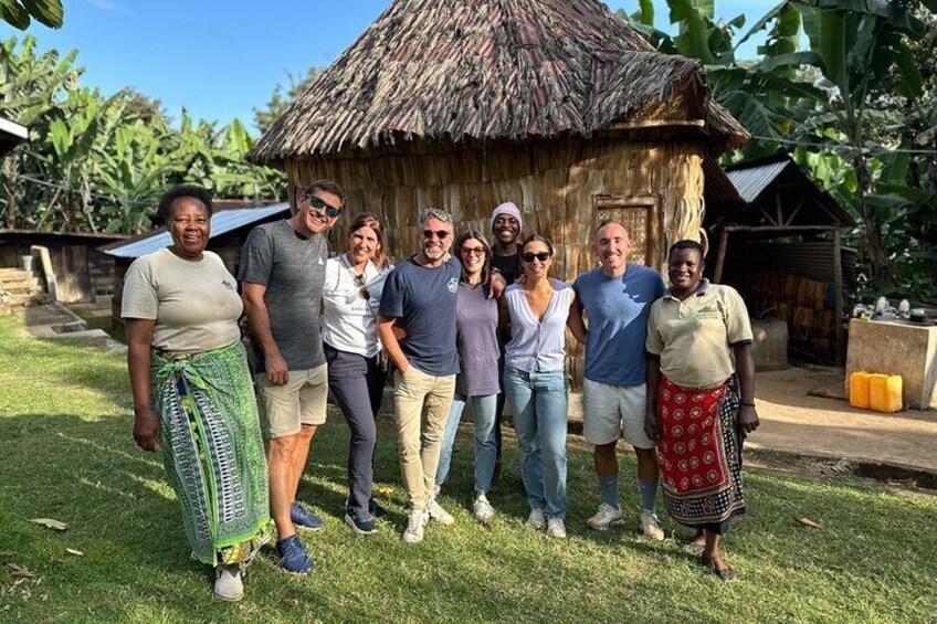 A group of people standing in front of a thatched-roof hut with a banana tree in the background. 3