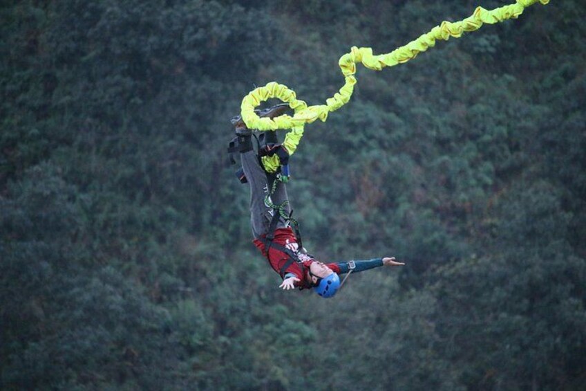 A person bungee jumping with a yellow bungee cord against a forested background. 1