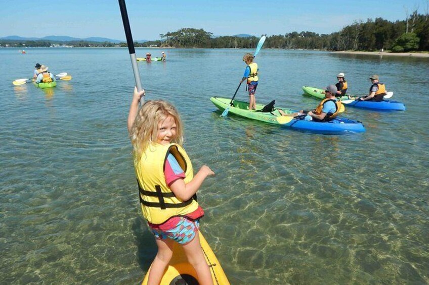 A person in a yellow kayak on a calm lake with other kayakers in the background. 4